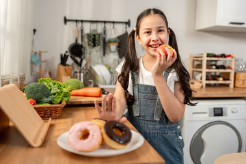 Adorable young kid girl rejecting junk food and eating apple in kitchen. 