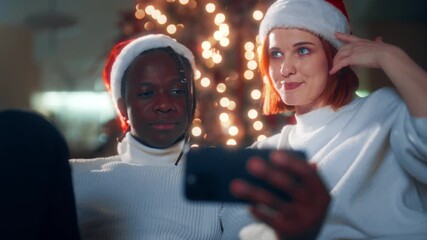 Happy multiethnic spouses celebrating Christmas, calling by video to friends. Portrait of african american husband and caucasian wife in Santa hats on head, modern technology for communication online - Powered by Adobe