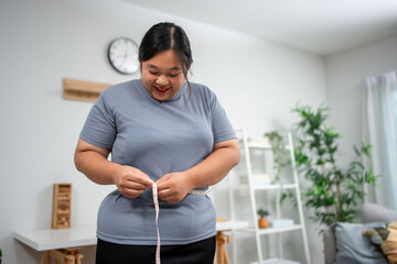 Asian young overweight woman measuring waist with tape measure at home. 
