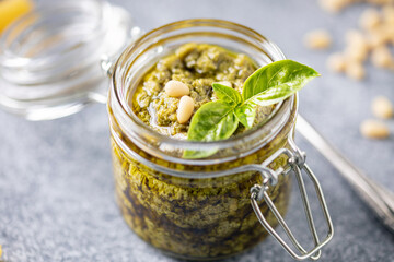 Sauce pesto with basil leaves, pine nuts and olive oil in jar on the table