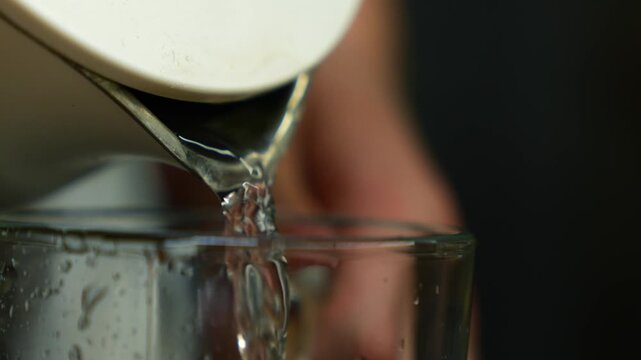 Electric kettle with hot water.
Boiled water from the kettle pours into a glass cup in the kitchen.
White electric kettle fills an empty cup with water