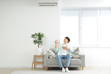 Young man resting on sofa in room with operating air conditioner