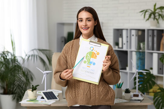 Female engineer with clipboard and wind turbine models on table in office - Powered by Adobe
