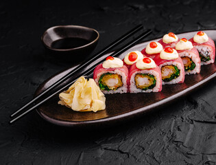 Delicious sushi rolls presented on a dark plate with garnishes and soy sauce