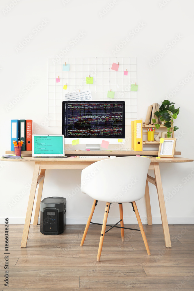 Poster programmer's workplace with computer monitor, laptop and pin board in light office