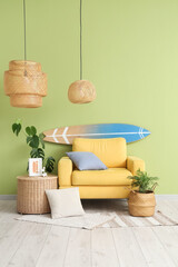 Comfortable yellow armchair with soft pillows and surfboard near green wall in living room