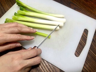 Woman with a hobby of cooking, cutting fresh spring onions on a cutting board