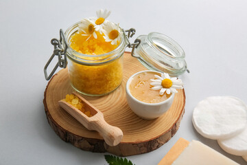Wooden round slice, chamomile flowers, scoop and jar with sea salt on white background, closeup
