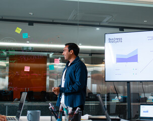 Confident Indian Businessman presenting ideas discussing strategy analysis financial data charts and graphs report on screen monitor with colleagues in boardroom office. Corporate Business meeting.