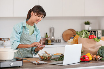 Young woman peppering vegetable salad in kitchen