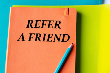 REFER A FRIEND - words on an orange notepad on a background of multi-colored folders