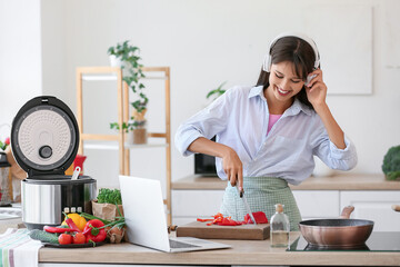 Young woman with headphones cutting bell pepper in kitchen