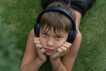 a young boy listening to music and gazing at the camera while lying on grass, concept of business audio entertainment, kids lifestyle, technology.