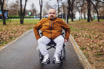 Portrait of paraplegic handicapped man in wheelchair in park. He is rolling on pathway.