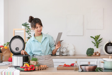 Young woman with tablet computer using multi cooker in kitchen