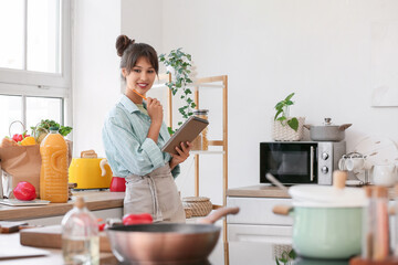 Thoughtful young woman with notebook and food from market in kitchen