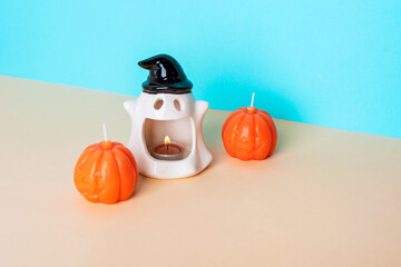 Ceramic ghost candle holder with burning tealight and two pumpkin shaped candles on blue and beige...