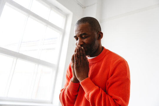 Mature man praying with hands clasped at home