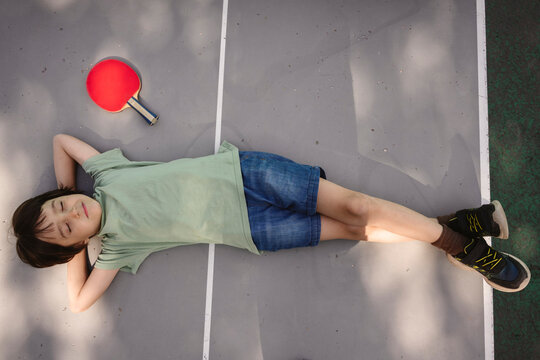 Child relaxing outdoors after playing ping pong with closed eyes