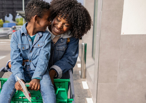 Happy mother with son sitting in shopping cart on sunny day