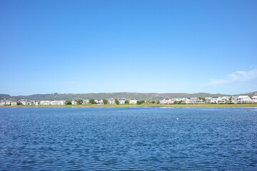 A calm lagoon with gentle rippling water reflecting the bright blue sky, with a charming coastal town and hills as backdrop. The peaceful scene with scenic view of travel and lifestyle