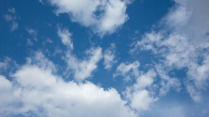 Obraz premium White clouds scattered across a bright, deep blue sky on a clear summer day.