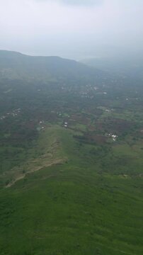 A drone shot captures the Nashik&ndash;Trimbak highway winding through lush greenery and towering mountains. The clear yet foggy sky adds a soft glow, bringing warmth and charm to the scenic landscape 4K