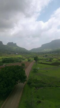 A forward drone shot follows a car driving along the Nashik&ndash;Trimbak highway, surrounded by lush greenery and rolling mountains. The clear blue sky adds warmth, highlighting the scenic beauty 4K