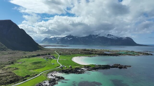 Drone flies forward over Hov beach on Gimsoy showing turquoise sea green hills road and peaks