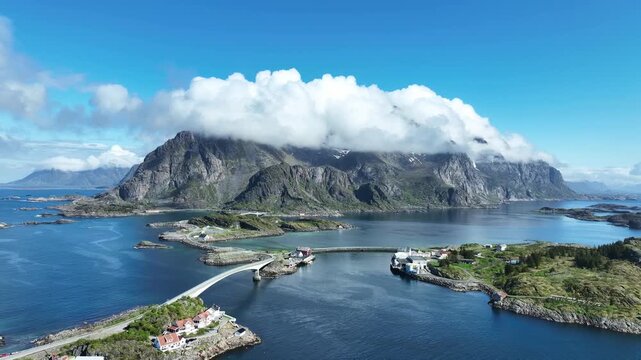 Drone flies forward over Henningsvaer road with bridges sea and mountains covered by clouds