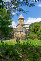 Obraz premium The outside of a monastery with a church and high stone walls. Green grass and trees. Hills, sky with clouds in the background. Pitareti monastery. Georgia