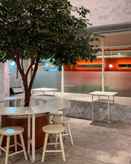 Modern cafe interior with a tree centerpiece, round table, and wooden stools, combining natural and minimalist industrial design.
