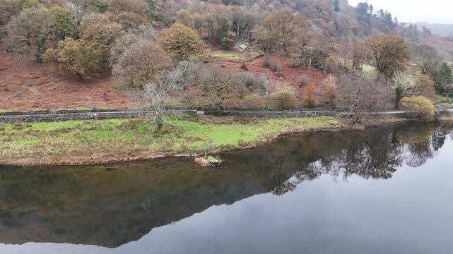 Rydal Water, A serene landscape captures a tranquil lake reflecting the autumnal foliage and distant mountains under a cloudy sky.