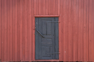 Minimalist black wooden door in red painted timber wall, reflecting ecological Nordic tradition of sustainable housing and simple rural architecture