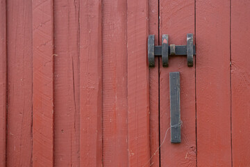 Close-up of metal latch on red-painted wooden door, ecological Nordic tradition of sustainable housing and simple rural architecture
