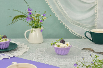 Vintage table decoration for anniversary, birthday, name day, Mother's Day or Grandma's Day. Cupcakes with cream and fruits, cups of coffee, retro napkins, wildflowers in white vase, mint tablecloth.
