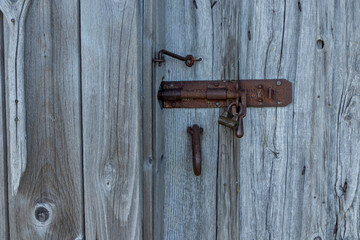 Metal latch on weathered gray wooden door. Natural timber aged by time, highlighting texture, patina, and rustic Nordic craftsmanship in rural architecture