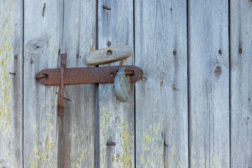 Metal latch on weathered gray wooden door. Natural timber aged by time, highlighting texture,...