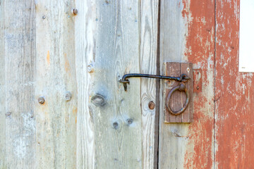 Close-up of metal latch on red-painted wooden door, ecological Nordic tradition of sustainable housing and simple rural architecture