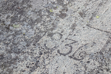 Close-up of weathered stone with carved historic dates and symbols. Deep grooves, rough texture, and aged patina, history, memory, and timeless northern heritage