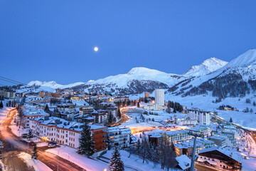 Aerial view of the snow-laden resort town nestled amidst towering, jagged peaks under a serene twilight sky, Sestriere, Piedmont, Italy.