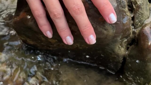 Female hand touching stone in river water, connection with nature, grounding and mindfulness