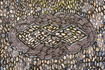 a cobblestone pavement featuring an intricate, symmetrical pattern with alternating dark and light stones forming a geometric design.