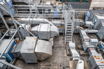 an industrial rooftop cluttered with various metallic ventilation systems, including large rectangular ducts and ladders