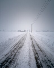 Snowy, empty road disappearing into a gray, misty winter landscape.  Power lines stretch across the scene