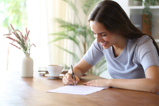 Happy woman signing paper document on wooden table at home