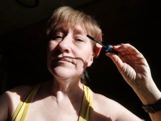 Middle-aged woman applies mascara while preparing for a lifestyle blog photo shoot at home during the afternoon