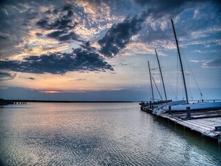 Sunset over a calm bay with sailboats and a dramatic sky.