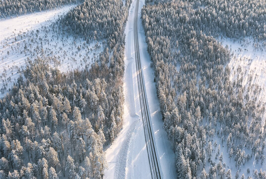 Aerial view of a stark, straight path cuts a swathe through a snow-laden forest, a study in contrasts of white and dark, Rovaniemi, Finland.