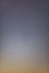 A tiny airplane flies through a vast, open sky at sunset. The minimalist composition with a gradient of warm and cool tones creates a peaceful and spacious atmosphere.